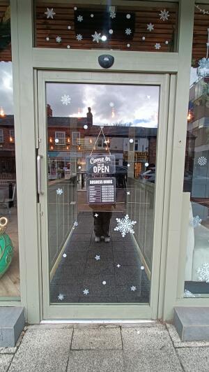 Grey framed glass door to venue. Push handle on left to open.