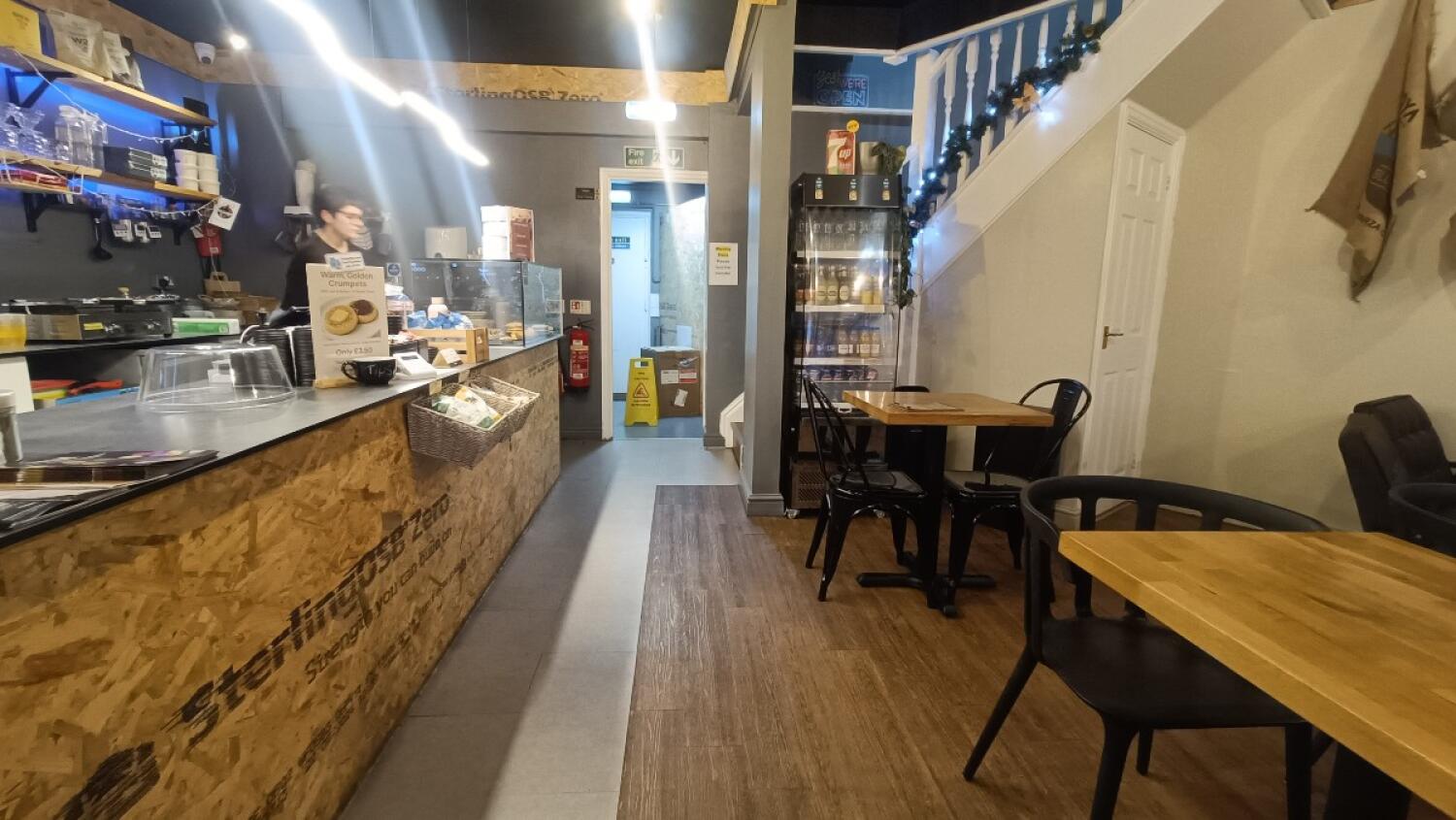 From counter facing right. Counter along left. Door to toilet at back. Tables and chairs on right.