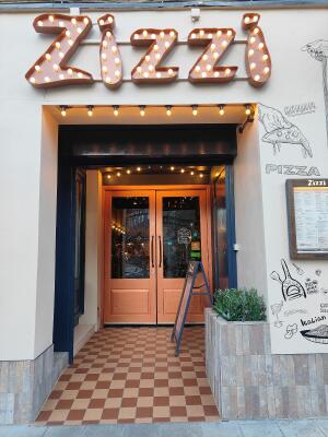 From sidewalk facing venue. Black framed archway ahead. Orange framed half glass doors ahead.