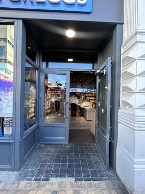 From sidewalk facing venue. Archway ahead. Glass doors with grey wooden frames at back. Pull from center to open.