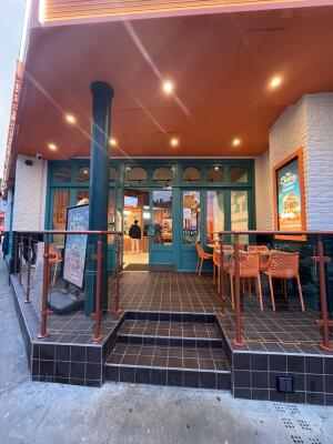 Path straight to blue doors at back. Glass dividing walls with orange metal frames on left and right.
