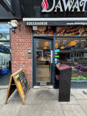 Glass door with black frame ahead. Push from right to open. A framed sign on left, desk with menus on right.