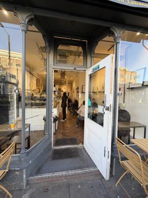 Archway with grey wooden frames ahead. Glass door with white frames at back. Pull from left to open.