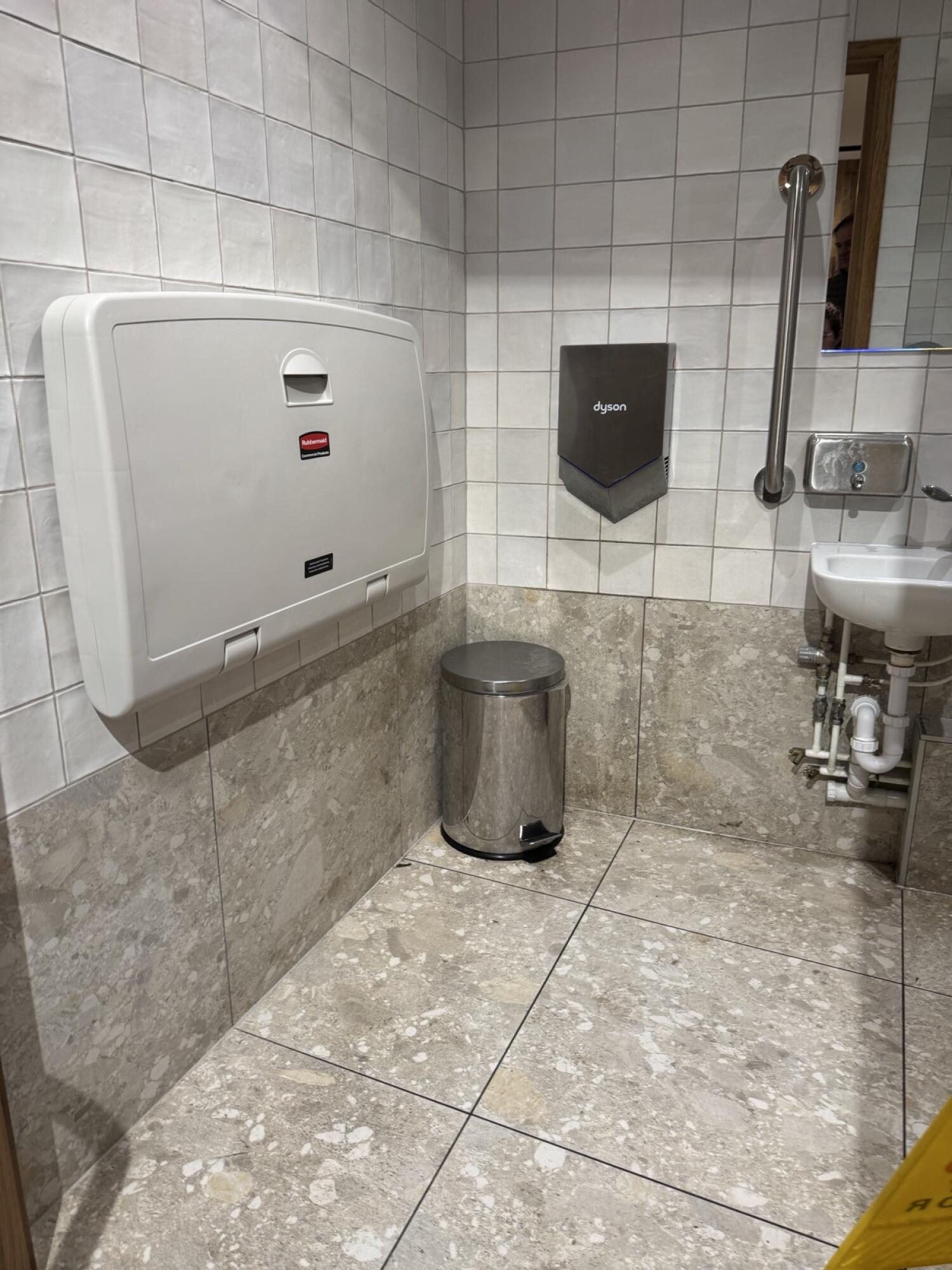 Baby changing station on left wall. Hand dryer on back wall. Sink on right wall.