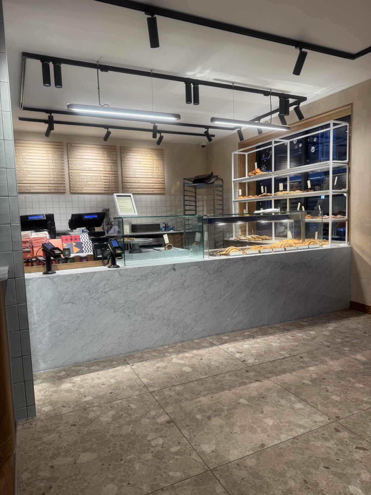 Counter with tills along left. Glass display counter with pastries at centre and right. Menu boards on back wall.