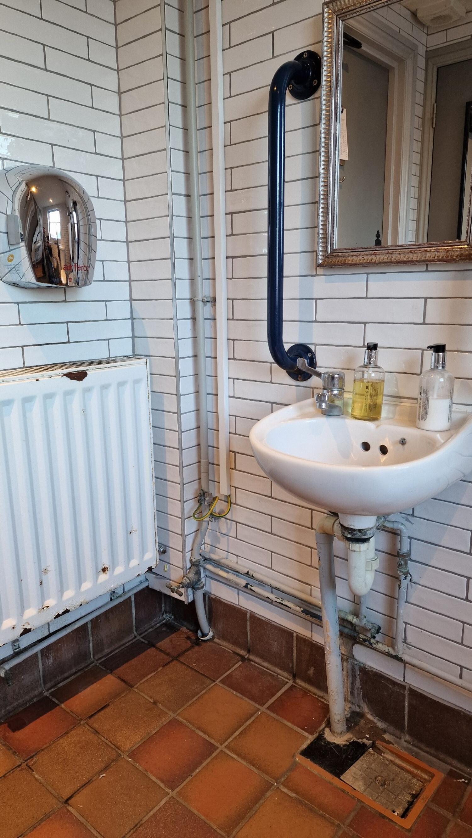 Sink on right wall with soap dispensers on top.  
Red emergency pull cord to left of sink.  