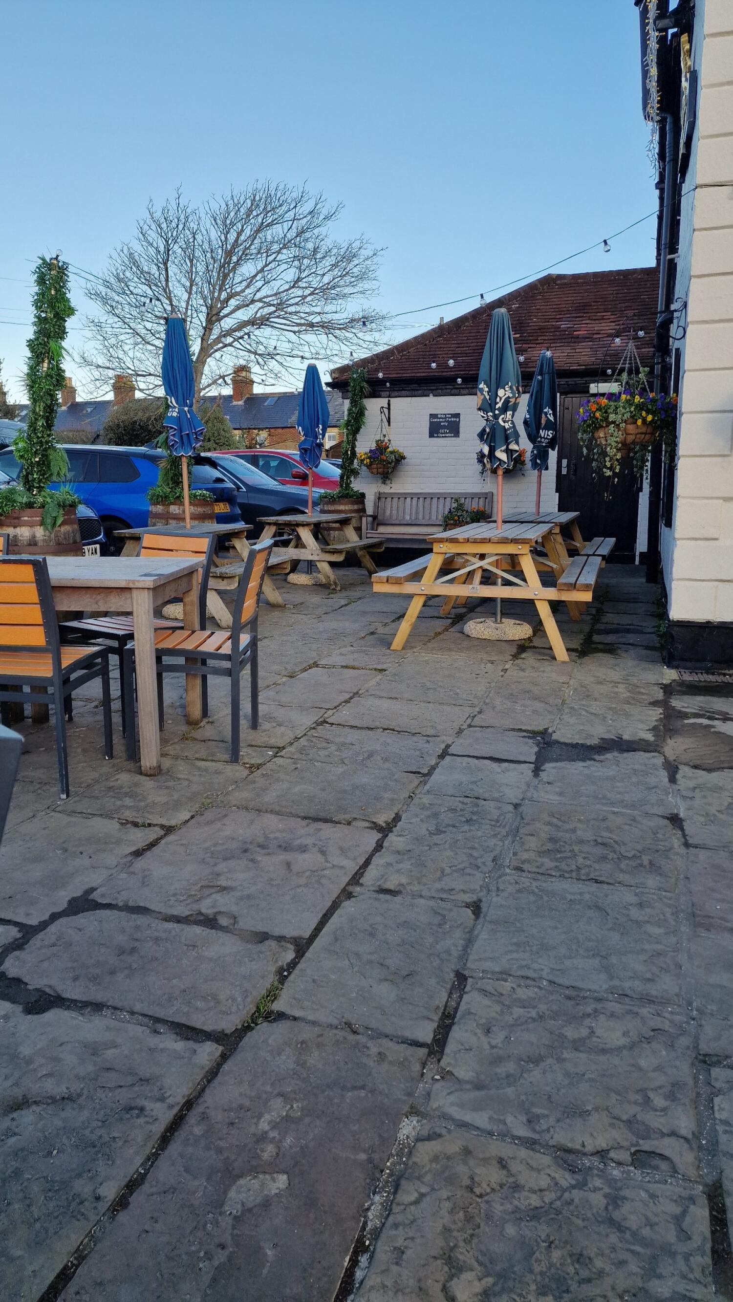 Tables with chairs along left. Picnic benches with parasols in centre. Bench seating against back wall.