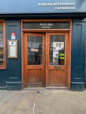 Blue frame brown wooden doors with glass panels in front. Gold handles in center. Push to open.