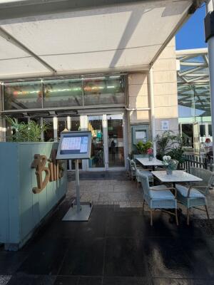 From sidewalk facing the venue. Menu on left. Entrance door behind at back. Tables and chairs on right.