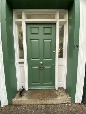 Green wooden door. Turn silver metal handle in centre and push from right to open.