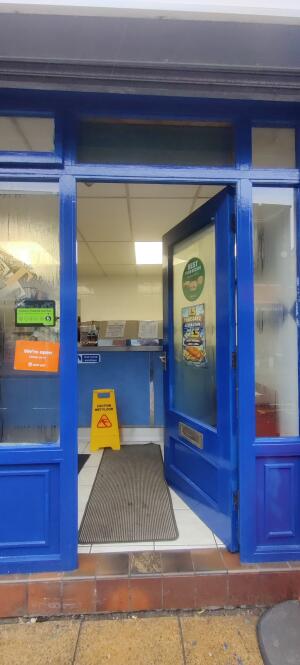Blue wooden framed glass door ahead. Turn and push metal handle from left to open.