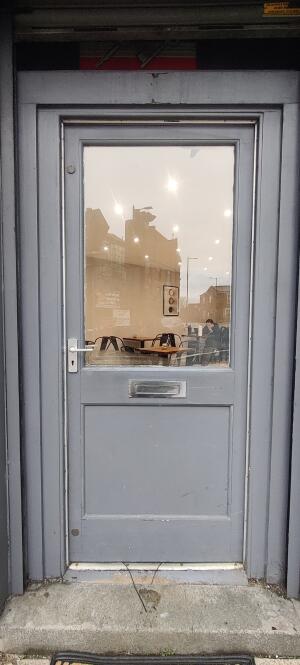 Grey wooden framed glass door ahead. Twist push metal handle at center.