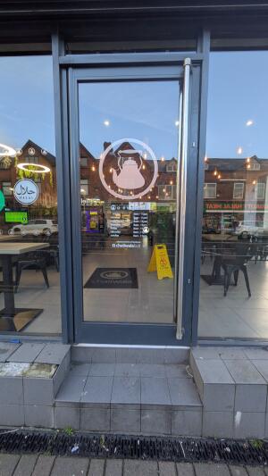 Grey metal-framed glass door. Pull from vertical handle on right to open. Two steps up to door.