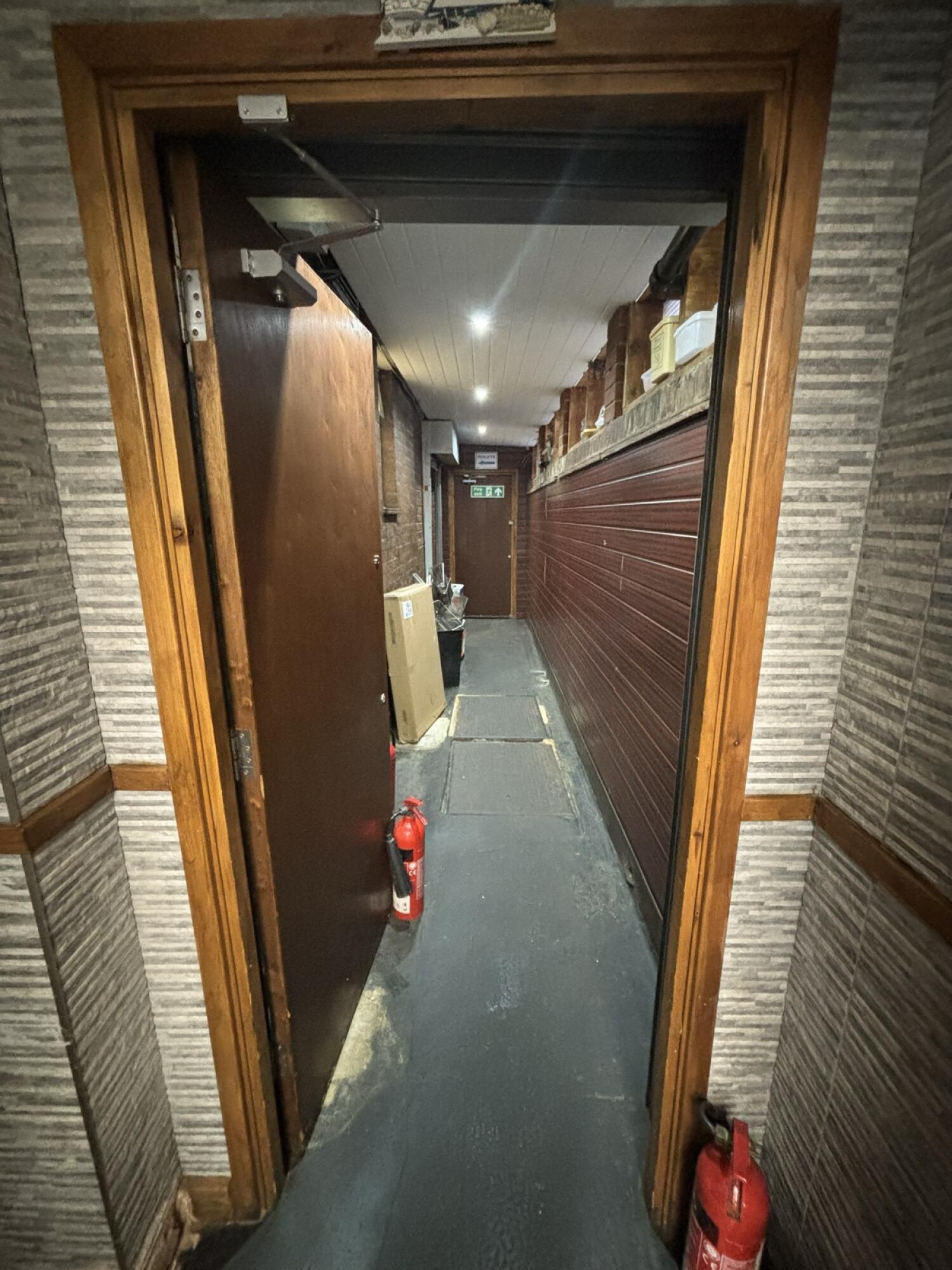 From archway facing straight. Brown door ahead to toilet. Push from right to open. Path ahead following door.