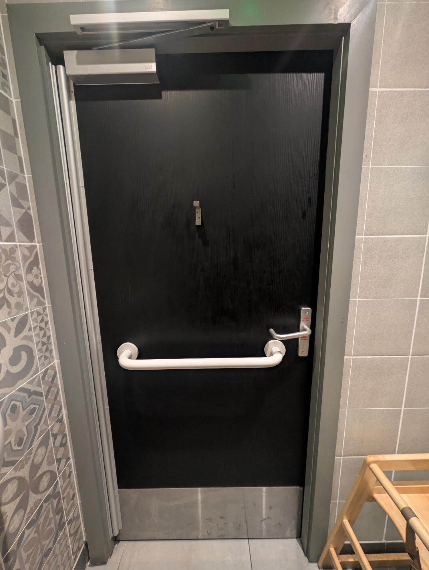 Back of bathroom door. High hook in center. White grab rail in middle. Silver handle on right. Push to open.