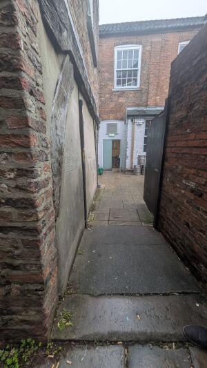 From back right of venue facing right. Narrow path between brick walls. Door ahead at end of path. Push on left to open