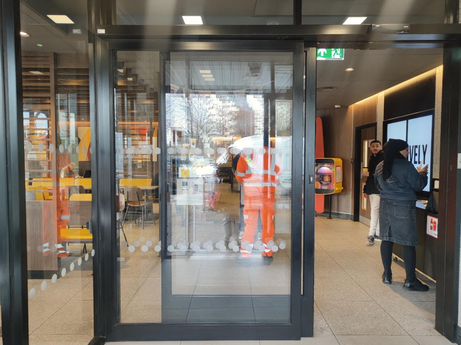 From doorway facing straight. Second grey framed automatic glass doors into venue ahead. Door slides left to open.