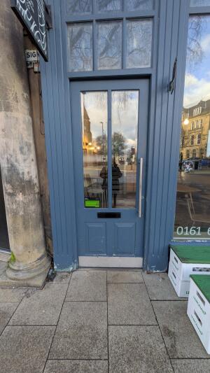 Blue wood-framed glass door. Push from metal handle on right to open.