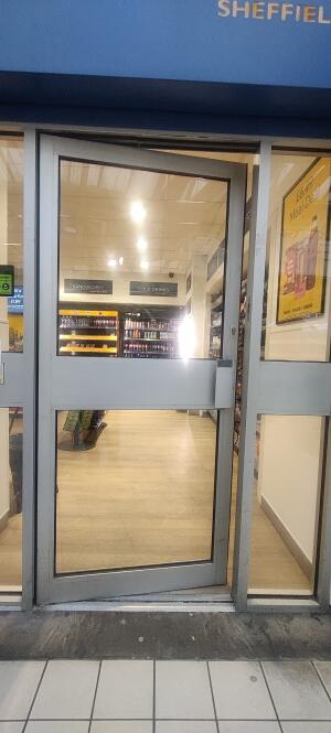 Grey metal framed glass door ahead. Push metal handle at right to open.