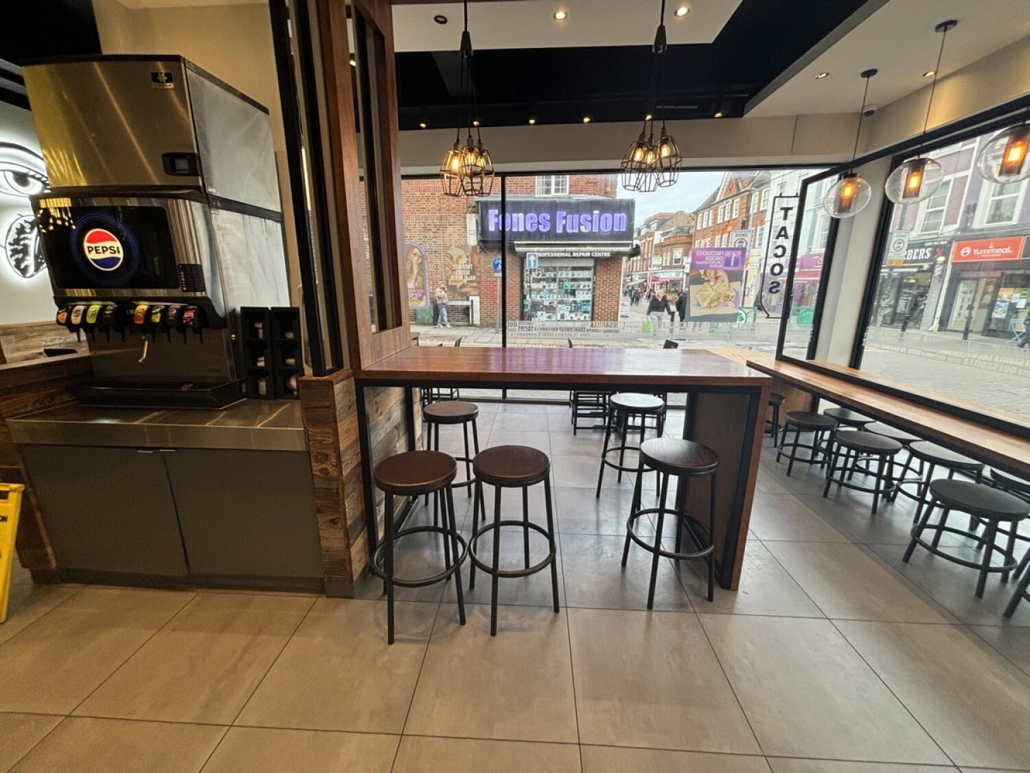 From opening facing straight. High tables and stools ahead. Drinks counter on left. Opening on right to more seating at back.