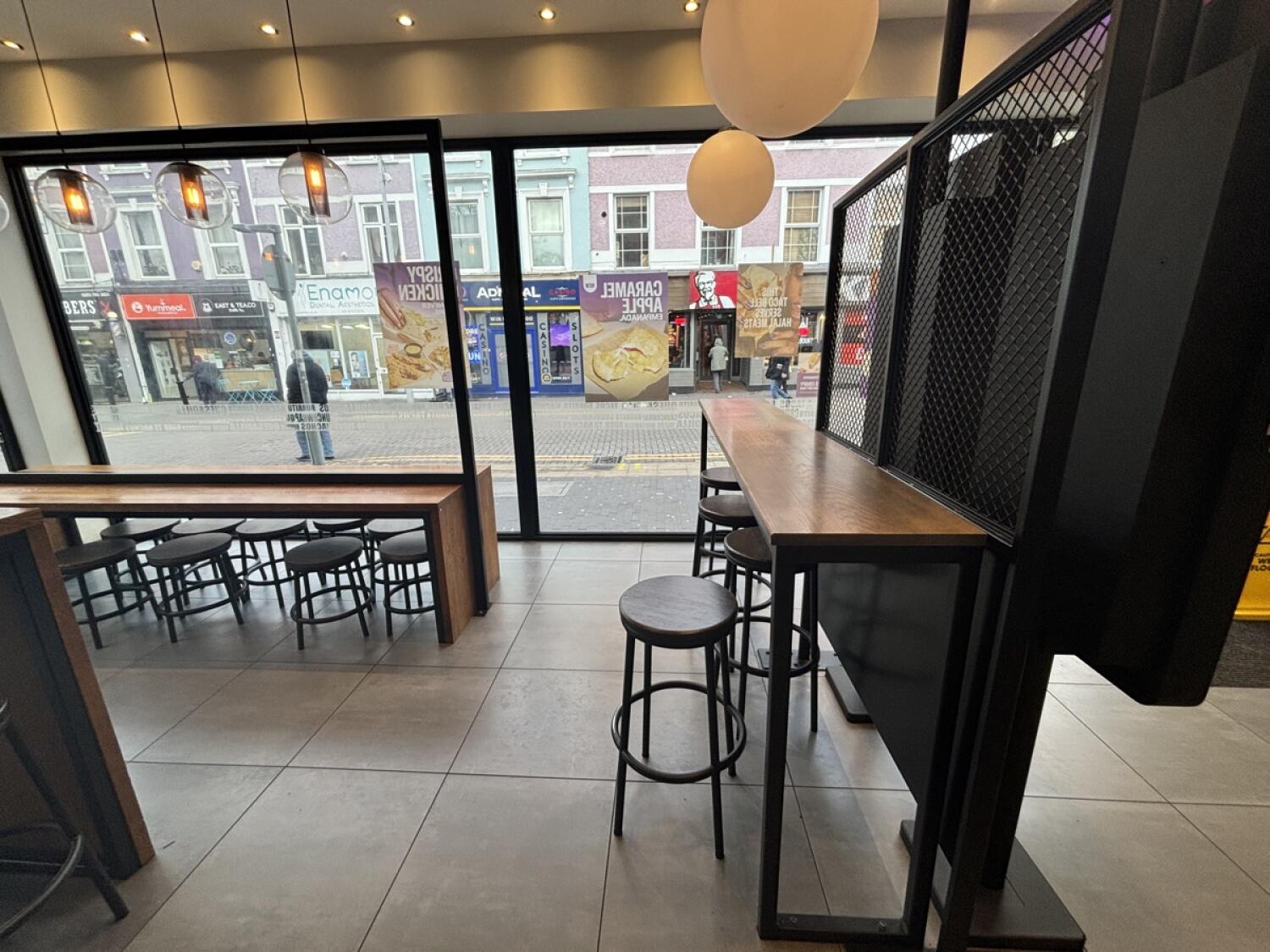 From opening facing right. High table and stools on right. Seated height table and stools at back. Second opening on left to more seating.