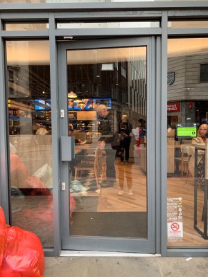 Glass door with grey metal frame. Push from grey metal handle on left to open.