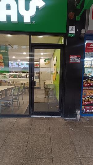 Black framed glass door to venue. Push handle on left to open.