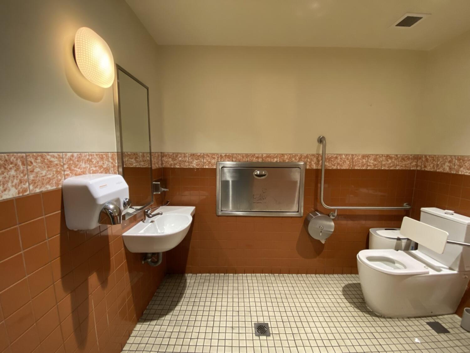 From door facing straight. Sink on back left wall. Baby changing station on back wall. Toilet at back right.