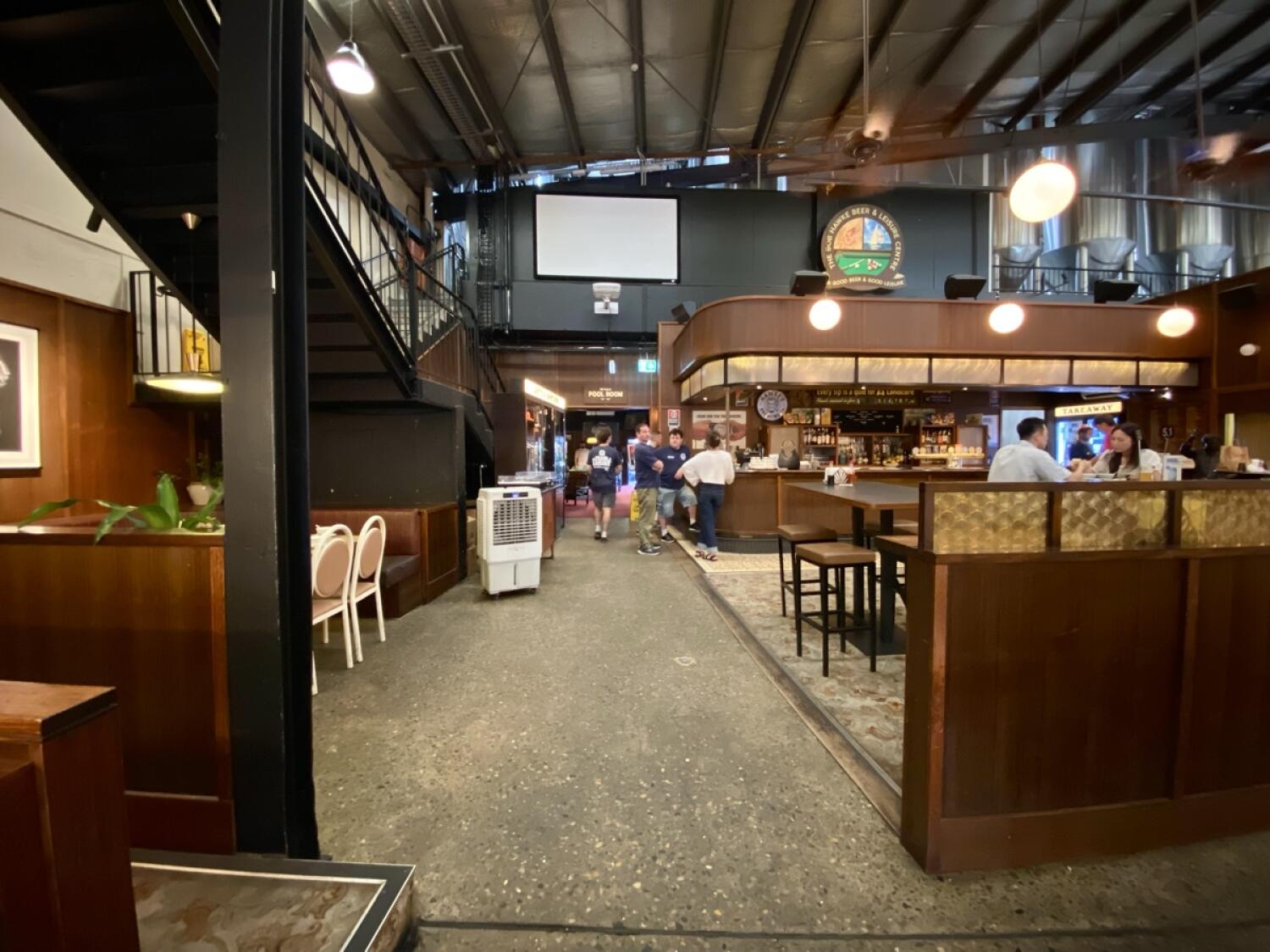 From end of path facing straight. Opening ahead to more seating space and bar counter. Path ahead leads to back space and upstairs space at back left.