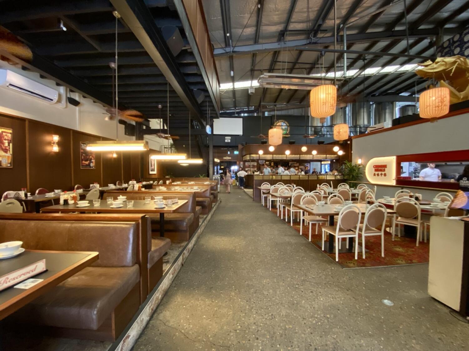 From after welcome desk facing straight. Booths along left wall. Tables and chairs along right. Path ahead to more seating space at back.