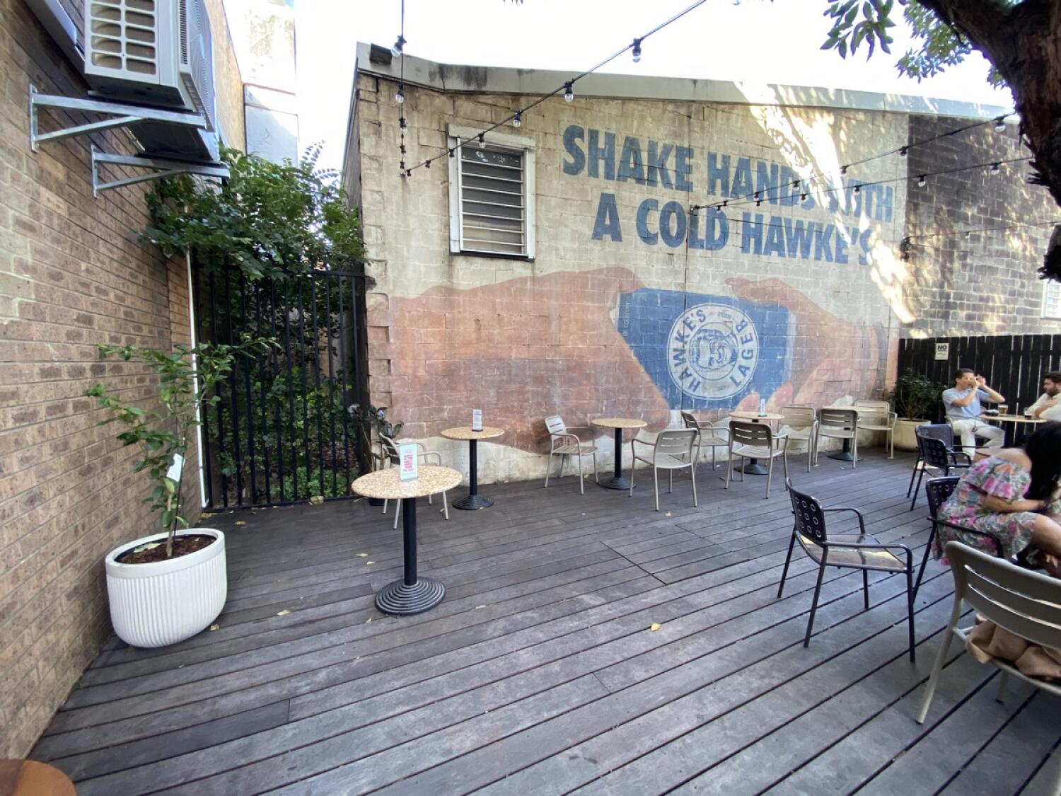 From door facing left. Tables and chairs spaced along back wall. Potted plant on left.