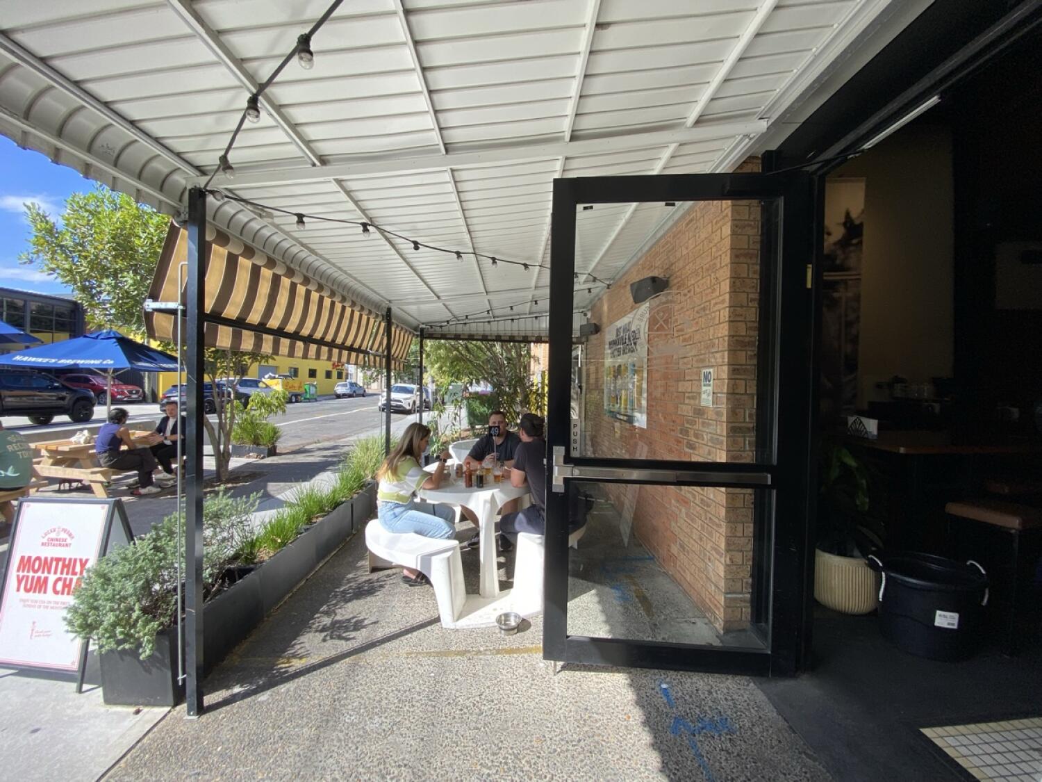 From entrance opening facing right. High tables and stools along left and right under canopy.