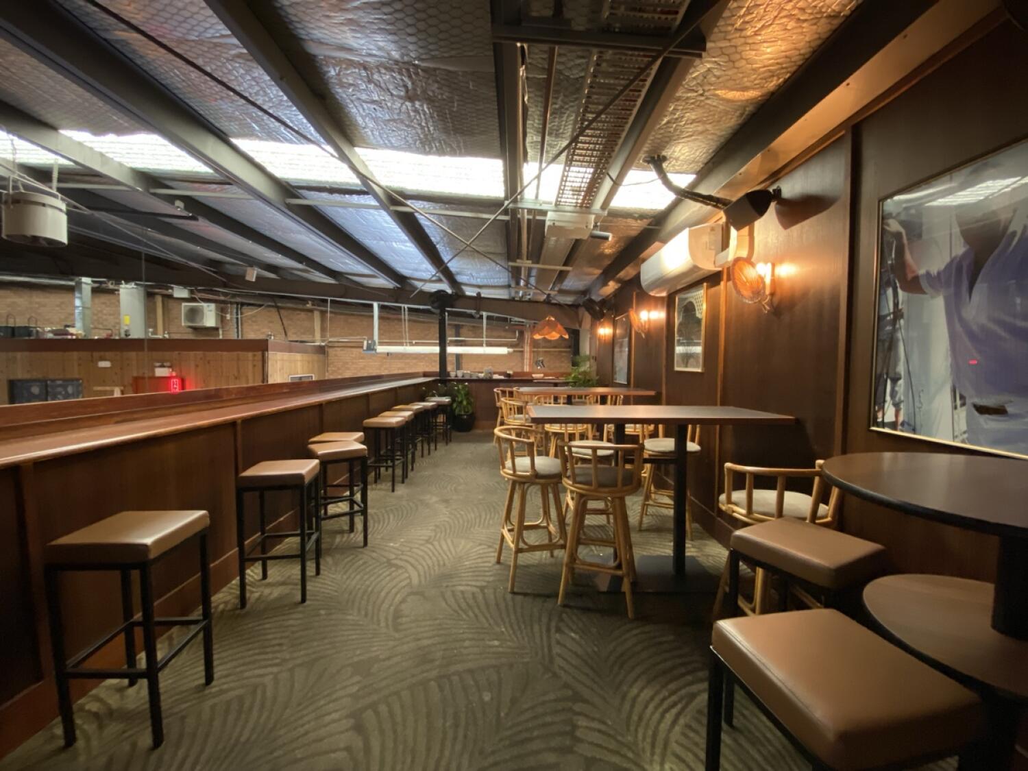 From top of steps facing straight. High tables and stools along left wall. More high tables and chairs along right.