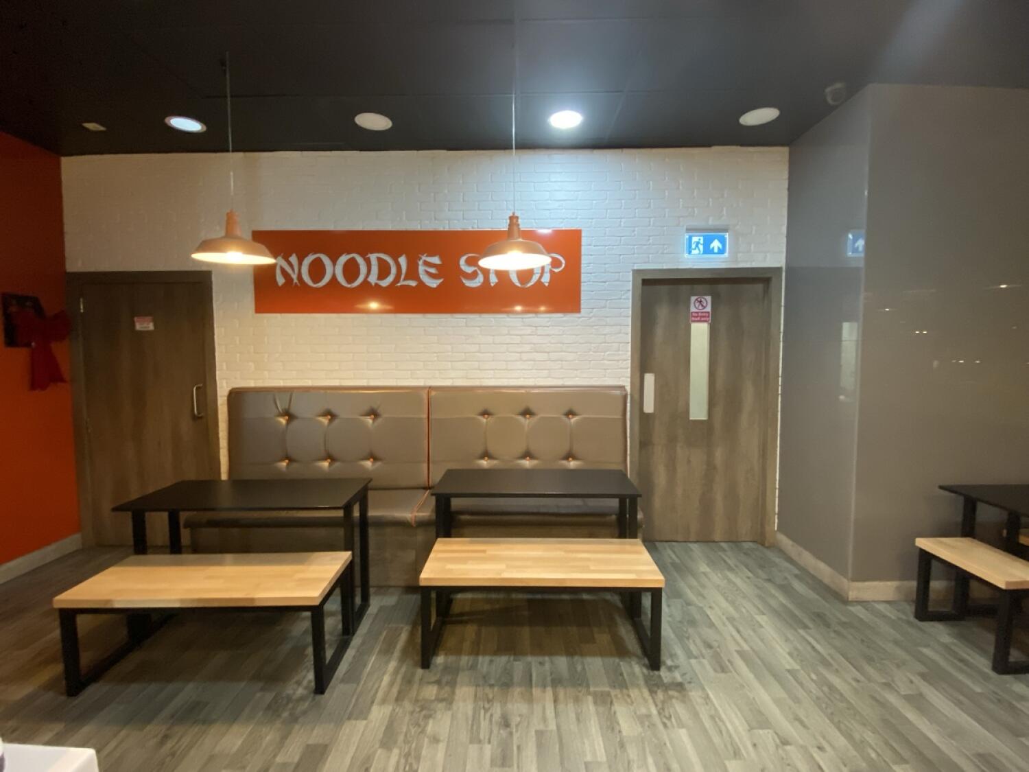 From end of counter facing straight. Bathroom at back left. Half booth, tables and benches along back wall.