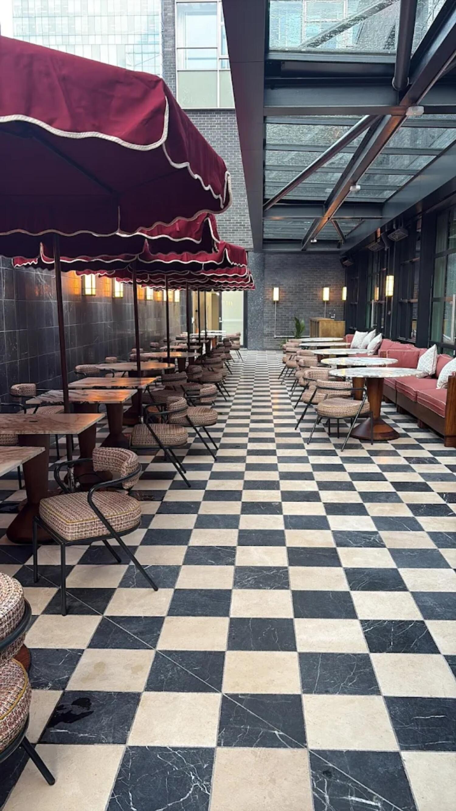 Tables and chairs along left under red parasols. Path in centre. Half booth seating with tables along right wall.
