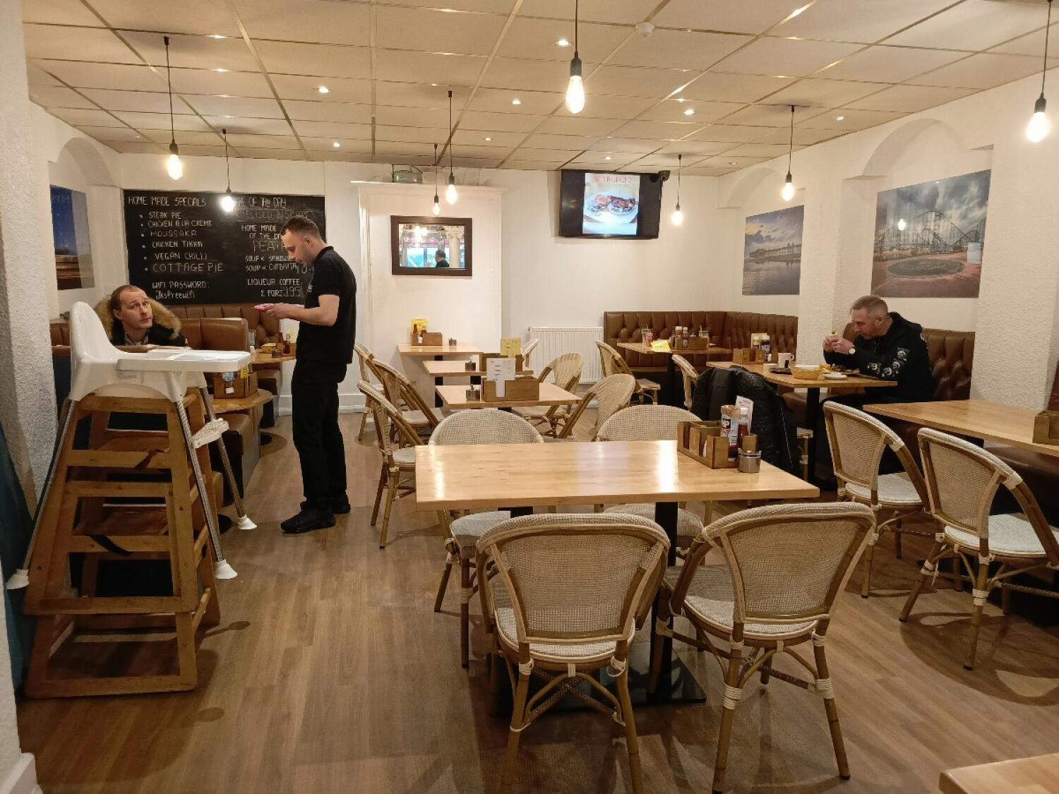 From archway facing straight. Half booths and tables along left. Tables and chairs at centre. Half booths, tables and chairs along right.