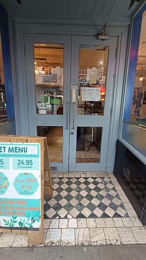 Grey-framed glass doors to venue. Pull handle in centre to open. A-frame board on left.