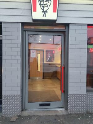Grey metal-framed glass door. Push from red handle on right to open.