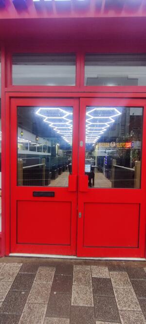 Red metal-framed glass doors ahead. Push from handles at centre to open.