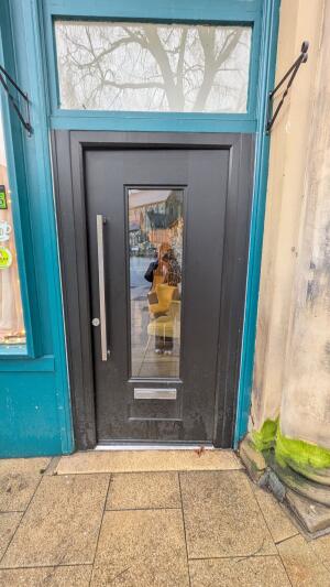 Black wooden door with central glass panel. Push from metal handle on left to open.