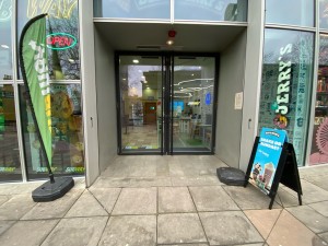 From pavement facing venue. Glass doors with black framing ahead. Pull from silver metal handles in centre to open.