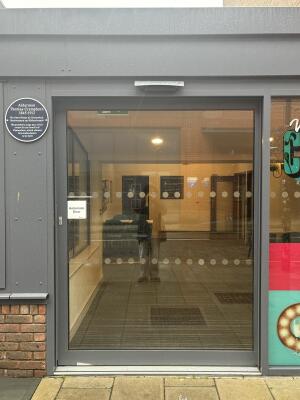 Grey metal-framed glass automatic door. Door slides left to open.