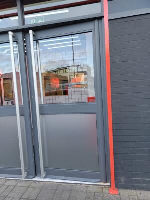 Grey metal-framed glass door ahead. Push from vertical handles at centre to open.