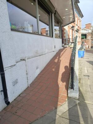 From street facing venue. Ramp leading up along building wall. Guardrails on right.