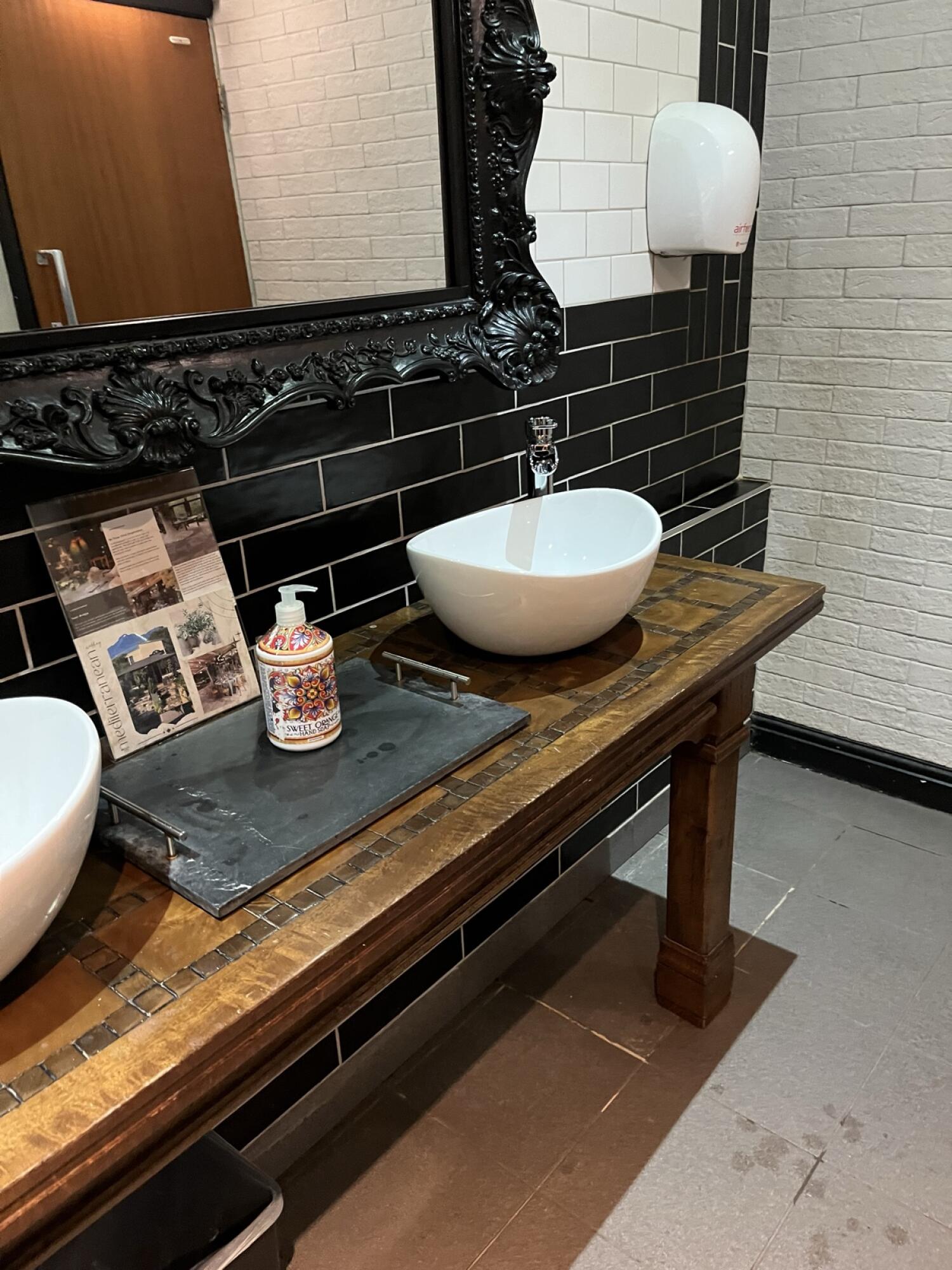 Two sinks along wooden counter. Soap dispenser between sinks. Paper towel dispenser on right wall.