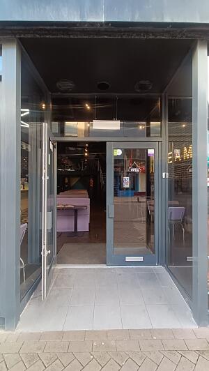 Grey metal-framed glass doors to venue. Pull from handle in centre to open.