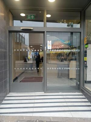 Grey metal-framed glass door ahead. Automatic door slides right to open.