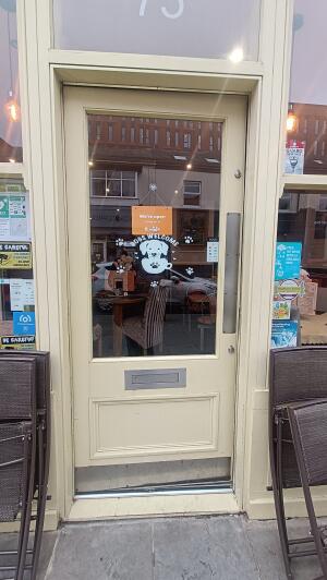 Cream wood-framed glass door to venue. Push from metal panel on right to open.