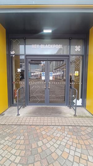 Dark grey metal-framed glass doors. Enter through doors opening from centre. Handrail on both sides.