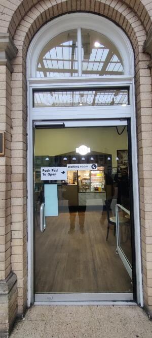 Glass door with white metal frame ahead. Push pad on right to open.